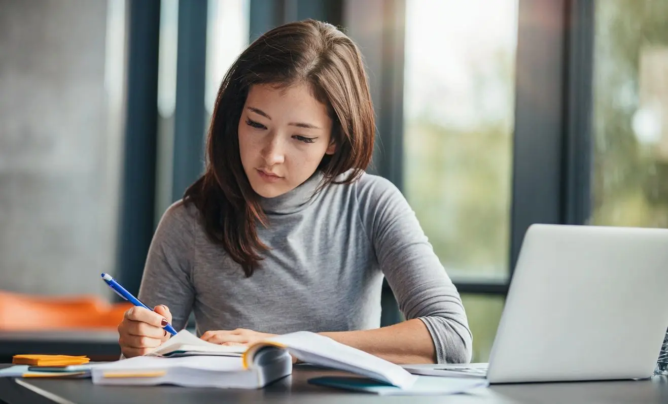 A woman sitting at a table writing on paper.