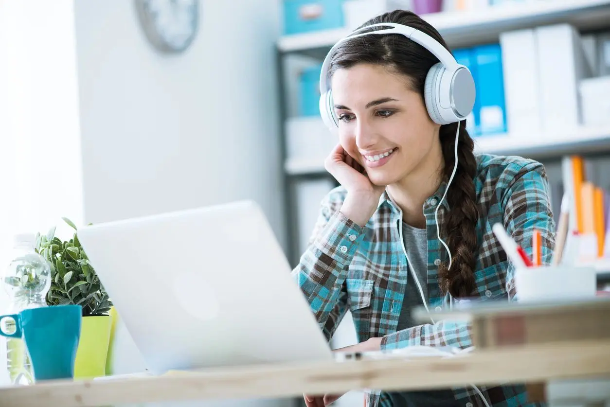 A woman with headphones on looking at her laptop.